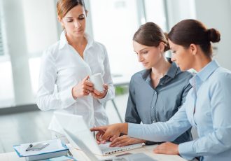 Successful women in business, they are working at office desk, pointing at computer screen and smiling
